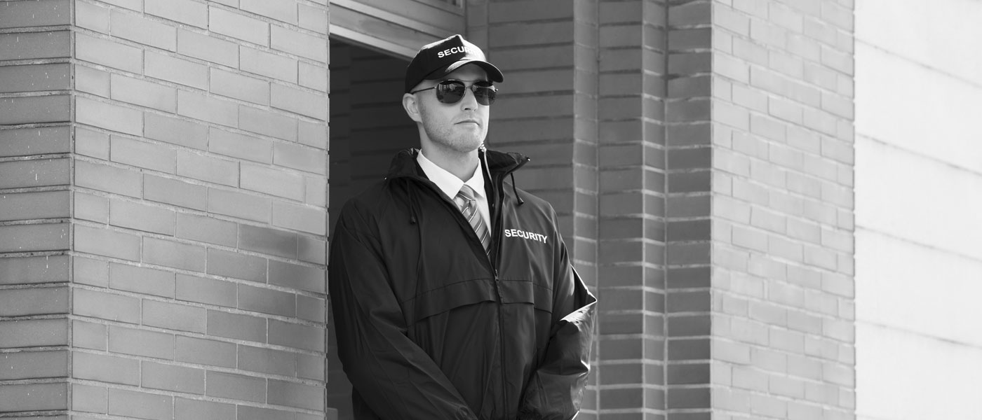 Agent de sécurité avec casquette et lunette de soleil devant une porte.
